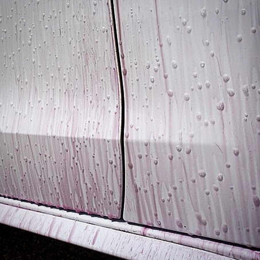 Close-up of a car's side with water droplets on a textured surface